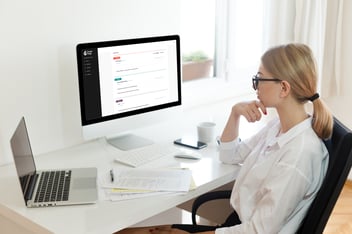 woman in glasses sitting at white desk looking at computer monitor